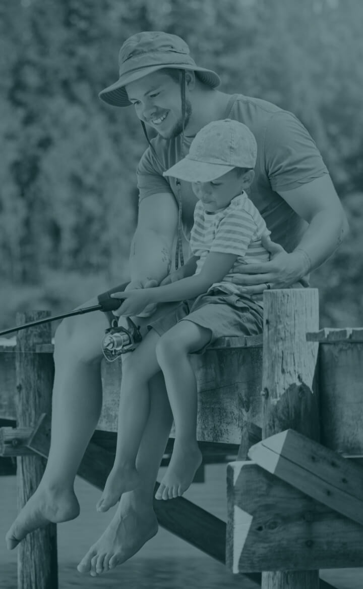 An adult and child fish together on a dock, enjoying peaceful moments near the Louisiana industrial corridor, both wearing hats.