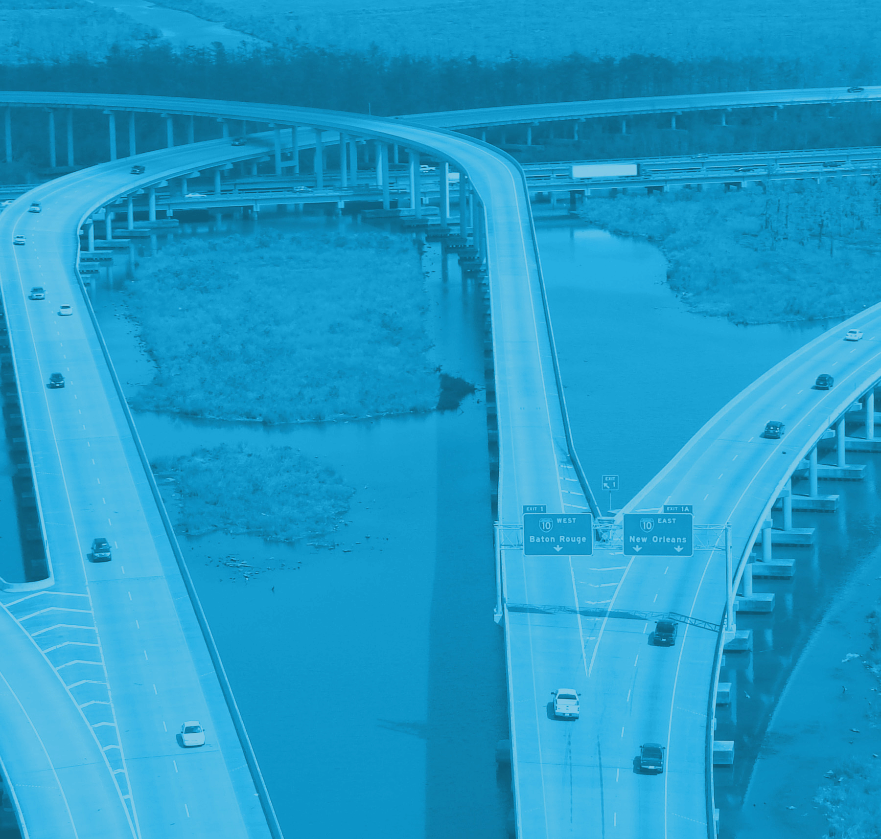 Aerial view of a highway interchange over water in the Louisiana industrial corridor, with signs for Baton Rouge and New Orleans.