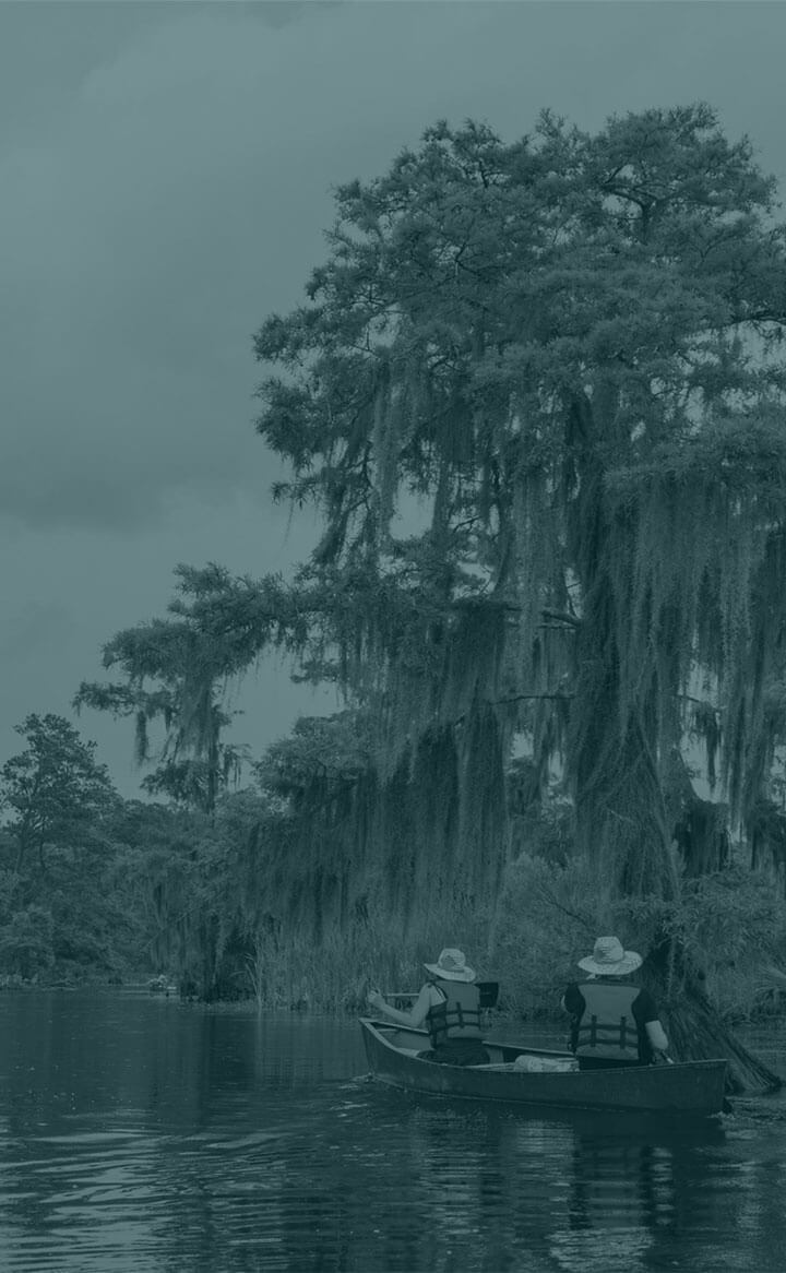 Two people in hats canoe on calm water near mossy trees, a peaceful scene far from Louisiana Chemical Association and cancer alley myths.