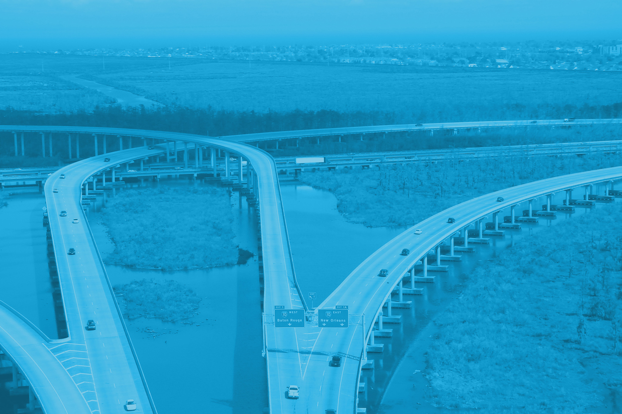 Aerial view of highways and overpasses in the Louisiana industrial corridor, with several cars crossing a vast wetland area.